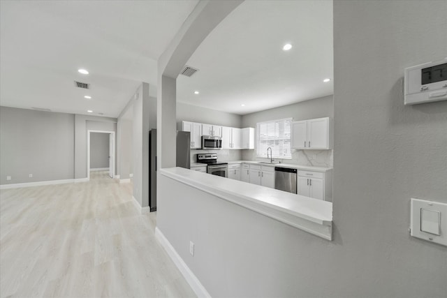 interior space featuring backsplash, appliances with stainless steel finishes, sink, light wood-type flooring, and white cabinets