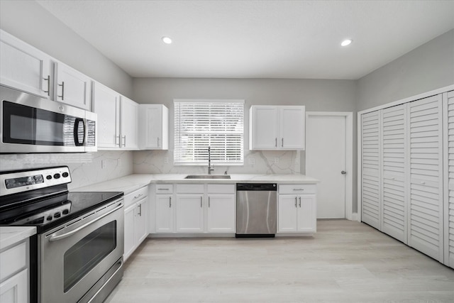 kitchen with sink, white cabinets, appliances with stainless steel finishes, light hardwood / wood-style floors, and tasteful backsplash