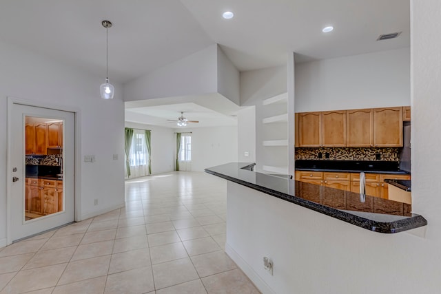 kitchen with light tile flooring, ceiling fan, backsplash, dark stone countertops, and decorative light fixtures