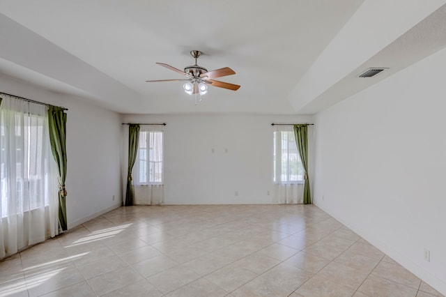 tiled spare room featuring ceiling fan, a healthy amount of sunlight, and a raised ceiling