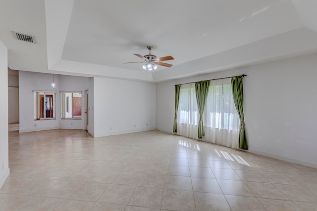 tiled empty room with ceiling fan and a raised ceiling