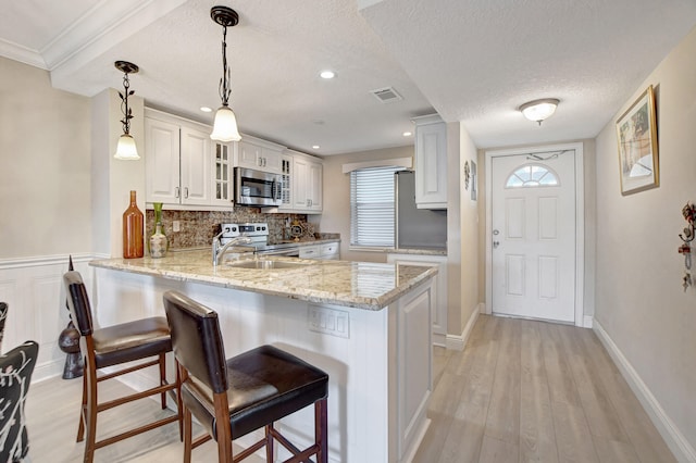 kitchen with decorative light fixtures, a textured ceiling, appliances with stainless steel finishes, white cabinets, and light wood-type flooring