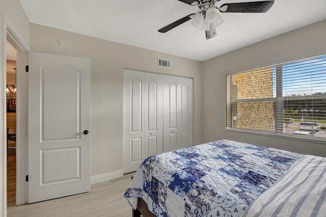 bedroom with light hardwood / wood-style floors, a closet, and ceiling fan with notable chandelier