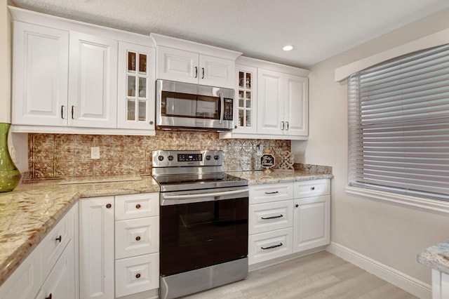 kitchen with stainless steel appliances, light stone countertops, tasteful backsplash, light hardwood / wood-style flooring, and white cabinets