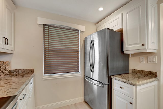 kitchen with light stone countertops, light hardwood / wood-style floors, stainless steel refrigerator, and white cabinetry