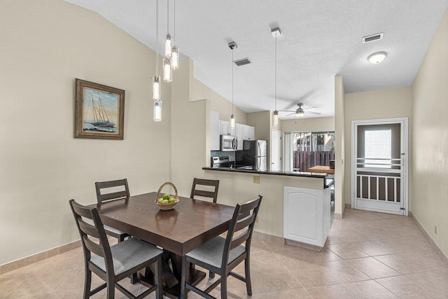 tiled dining space featuring ceiling fan, vaulted ceiling, and a textured ceiling