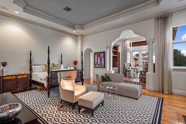 bedroom featuring crown molding, decorative columns, a tray ceiling, and light wood-type flooring