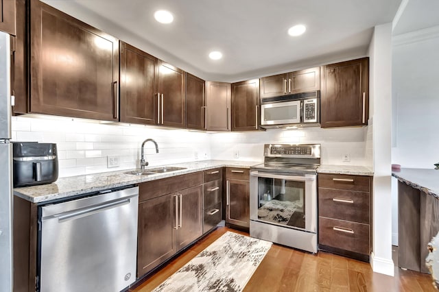 kitchen with light stone countertops, decorative backsplash, stainless steel appliances, sink, and light hardwood / wood-style flooring