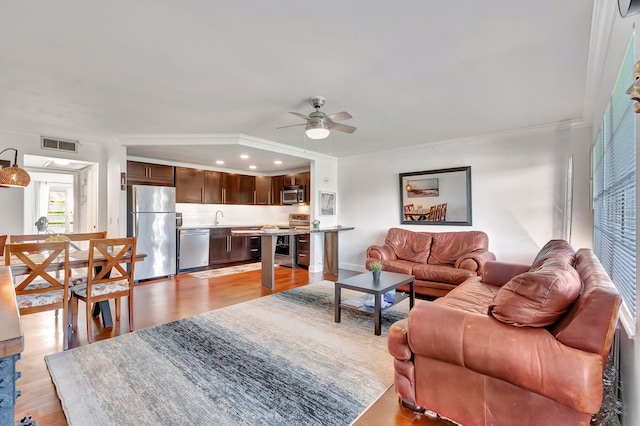 living room with light hardwood / wood-style floors, ceiling fan, crown molding, and sink