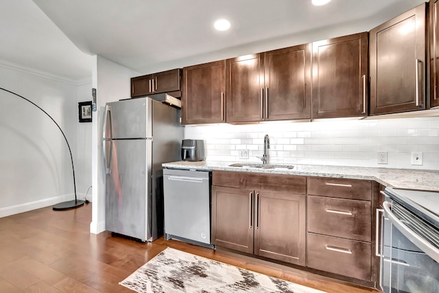 kitchen with appliances with stainless steel finishes, light stone counters, crown molding, sink, and light hardwood / wood-style floors