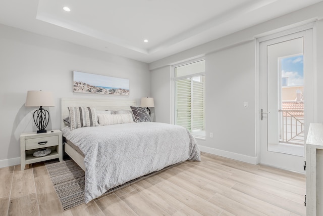 bedroom with a raised ceiling, access to exterior, and light wood-type flooring