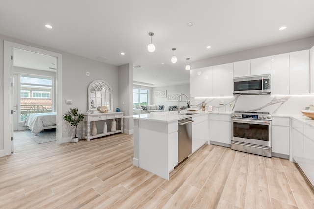 kitchen featuring kitchen peninsula, white cabinetry, light hardwood / wood-style flooring, stainless steel appliances, and pendant lighting