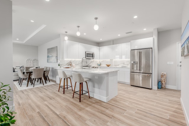 kitchen with pendant lighting, white cabinets, backsplash, light hardwood / wood-style floors, and stainless steel appliances