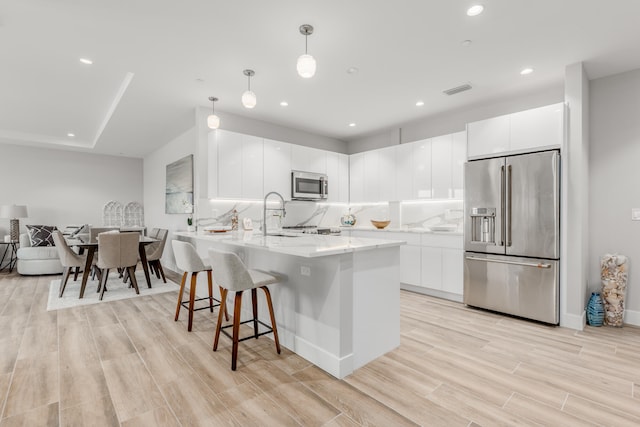 kitchen with white cabinets, light hardwood / wood-style floors, decorative light fixtures, and appliances with stainless steel finishes