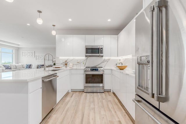 kitchen featuring kitchen peninsula, sink, white cabinets, appliances with stainless steel finishes, and light hardwood / wood-style flooring