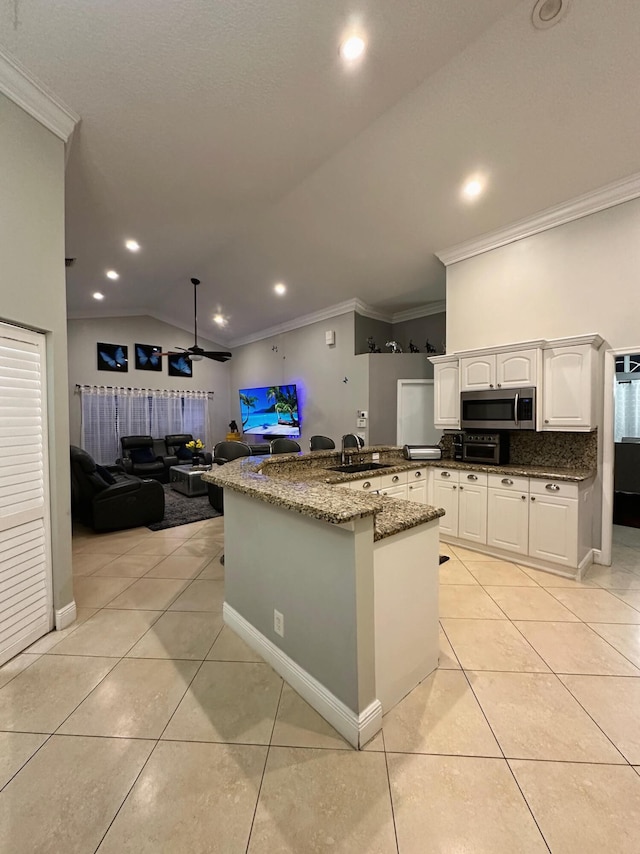 kitchen with dark stone counters, vaulted ceiling, light tile patterned flooring, crown molding, and white cabinetry