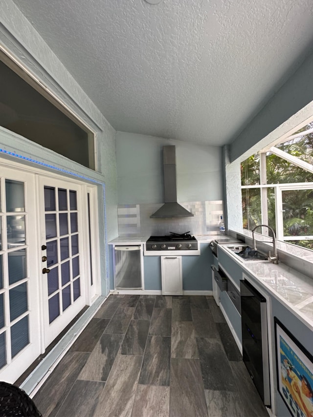 kitchen with light stone counters, a textured ceiling, stainless steel refrigerator, fridge, and wall chimney exhaust hood