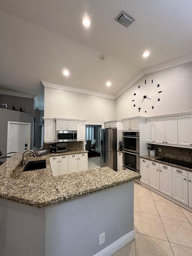 kitchen featuring stainless steel appliances, white cabinetry, backsplash, sink, and vaulted ceiling