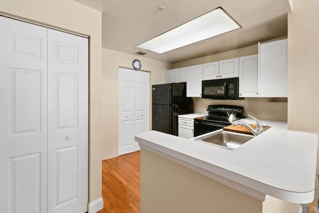 kitchen with kitchen peninsula, sink, white cabinets, black appliances, and light wood-type flooring