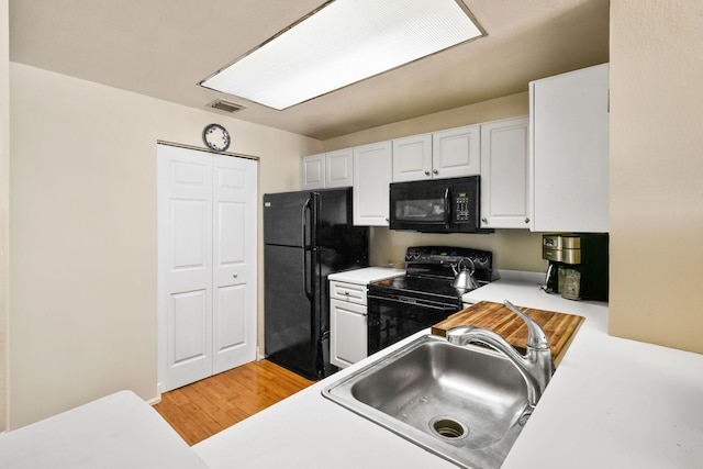 kitchen featuring white cabinetry, black appliances, sink, and light hardwood / wood-style flooring