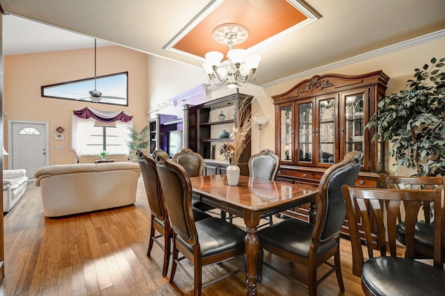 dining room with wood-type flooring, lofted ceiling, a tray ceiling, and ceiling fan with notable chandelier