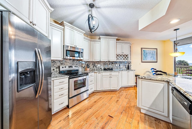 kitchen featuring light stone countertops, appliances with stainless steel finishes, light wood-type flooring, pendant lighting, and white cabinets