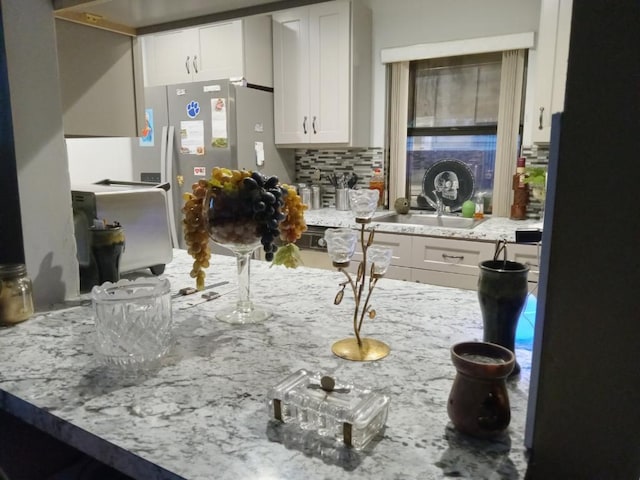 kitchen featuring white cabinetry, backsplash, sink, light stone counters, and stainless steel refrigerator