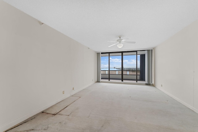 carpeted empty room with floor to ceiling windows, a textured ceiling, and ceiling fan