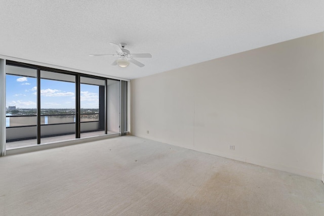 carpeted spare room featuring expansive windows, a textured ceiling, a water view, and ceiling fan