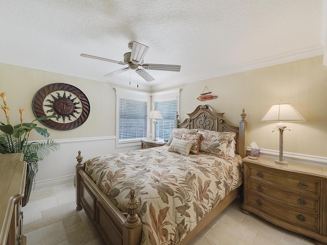 bedroom with a wainscoted wall, a textured ceiling, crown molding, and ceiling fan