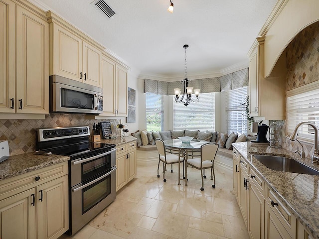 kitchen featuring visible vents, cream cabinetry, a sink, appliances with stainless steel finishes, and a chandelier