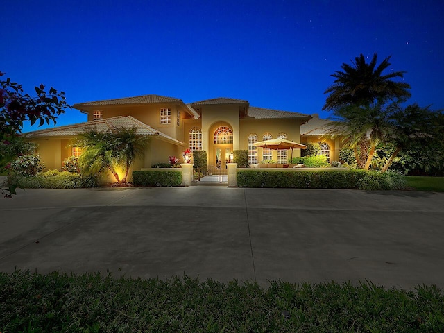 mediterranean / spanish-style home featuring stucco siding, a tile roof, and curved driveway