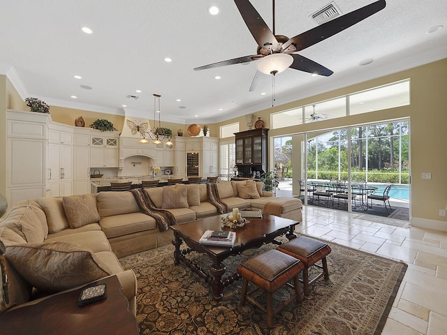 living area with visible vents, baseboards, ceiling fan, ornamental molding, and stone tile flooring