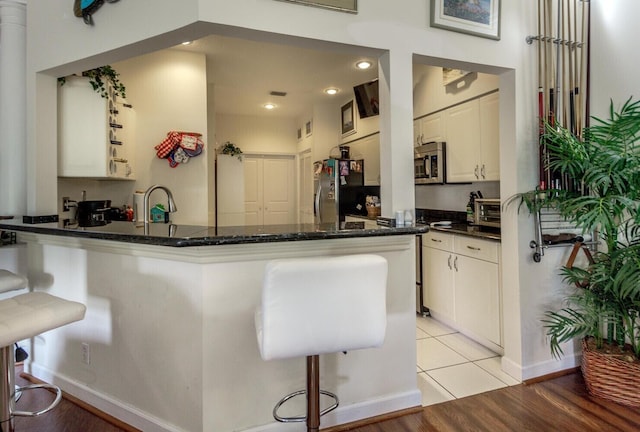 kitchen featuring dark stone countertops, kitchen peninsula, light tile patterned flooring, a breakfast bar area, and stainless steel appliances