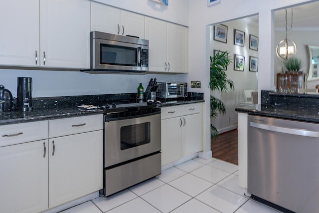 kitchen with white cabinetry, hanging light fixtures, stainless steel appliances, light tile patterned floors, and dark stone counters