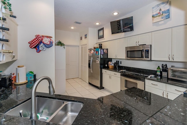 kitchen with light tile patterned floors, appliances with stainless steel finishes, a textured ceiling, white cabinets, and sink