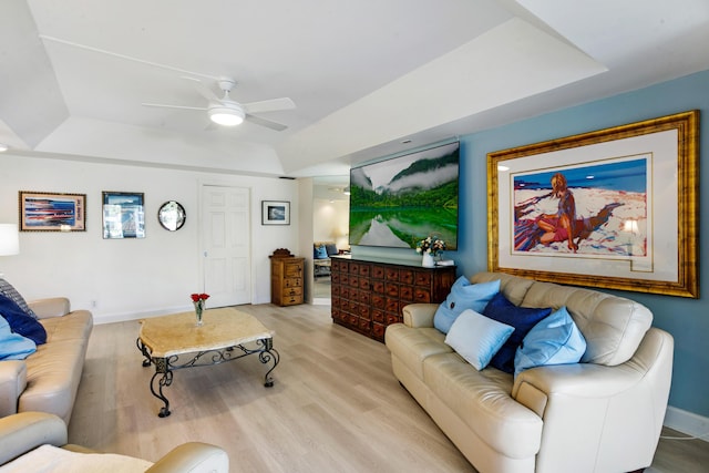 living room with ceiling fan, a raised ceiling, and light wood-type flooring