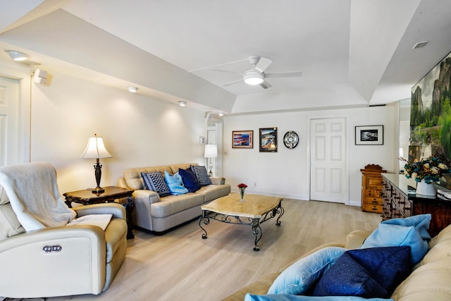 living room featuring ceiling fan, light wood-type flooring, and a tray ceiling