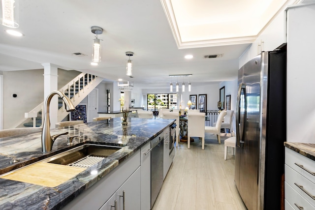 kitchen featuring stainless steel appliances, sink, pendant lighting, dark stone countertops, and white cabinetry