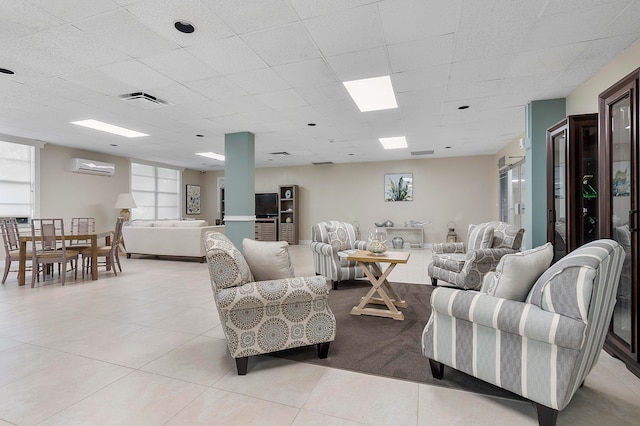 living room with a wall unit AC, a paneled ceiling, and light tile patterned flooring