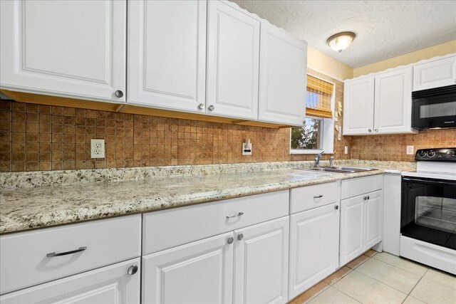 kitchen with electric range oven, sink, light tile patterned flooring, a textured ceiling, and white cabinets