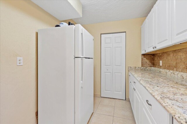 kitchen featuring white cabinets, white fridge, decorative backsplash, light stone counters, and light tile patterned floors