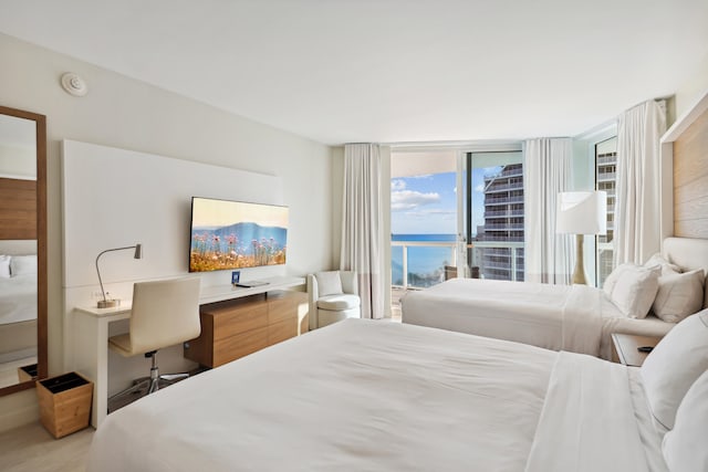 bedroom with expansive windows, light hardwood / wood-style floors, and a water view