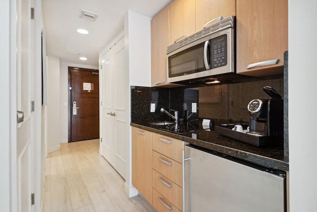 kitchen with light brown cabinetry, tasteful backsplash, light hardwood / wood-style floors, and dark stone counters