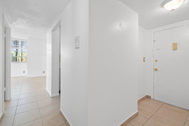 corridor with a textured ceiling and light tile floors