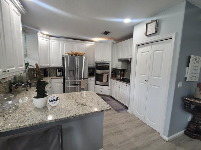 kitchen featuring appliances with stainless steel finishes, tasteful backsplash, white cabinets, light hardwood / wood-style floors, and light stone countertops