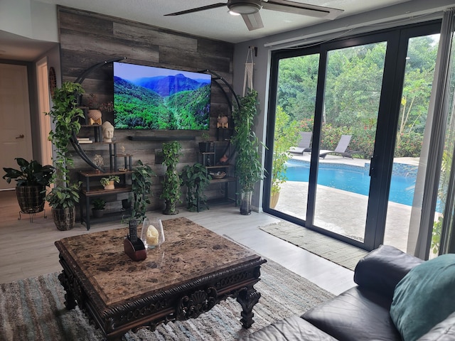 living room featuring wooden walls, a textured ceiling, ceiling fan, and light wood-type flooring