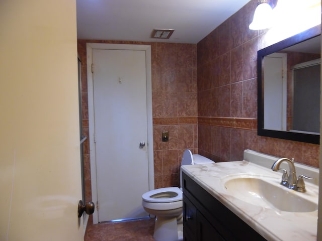 bathroom with tile floors, vanity with extensive cabinet space, toilet, and tile walls