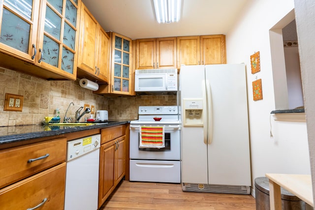 kitchen with light hardwood / wood-style flooring, sink, dark stone counters, white appliances, and decorative backsplash