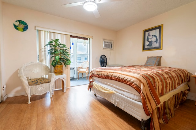 bedroom featuring ceiling fan, light hardwood / wood-style floors, a textured ceiling, and a wall unit AC